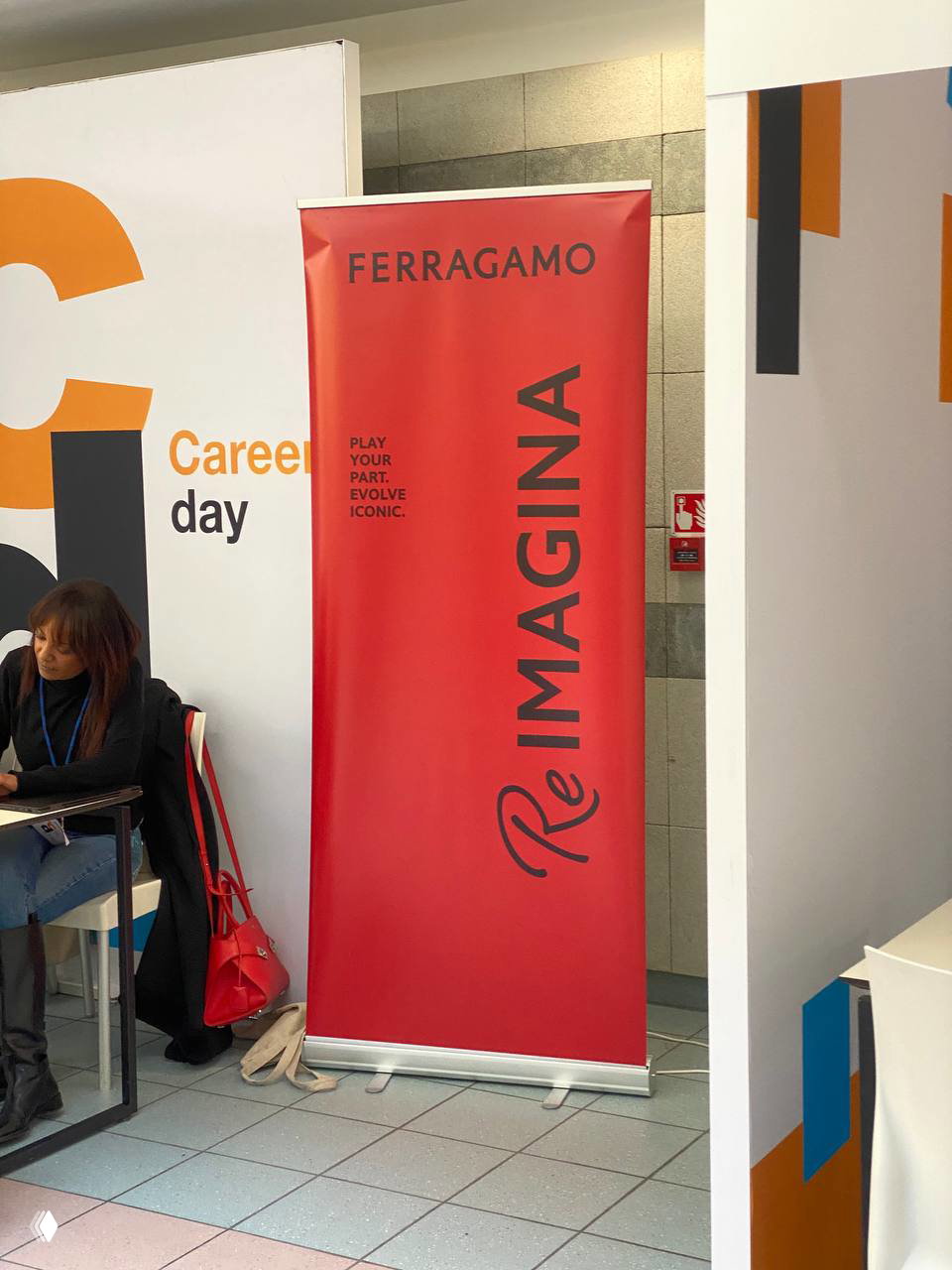 Красный ролл-ап Ferragamo на Career Day рядом с информационными стендами; видно брендовый баннер и элементы оформления павильона работодателя.