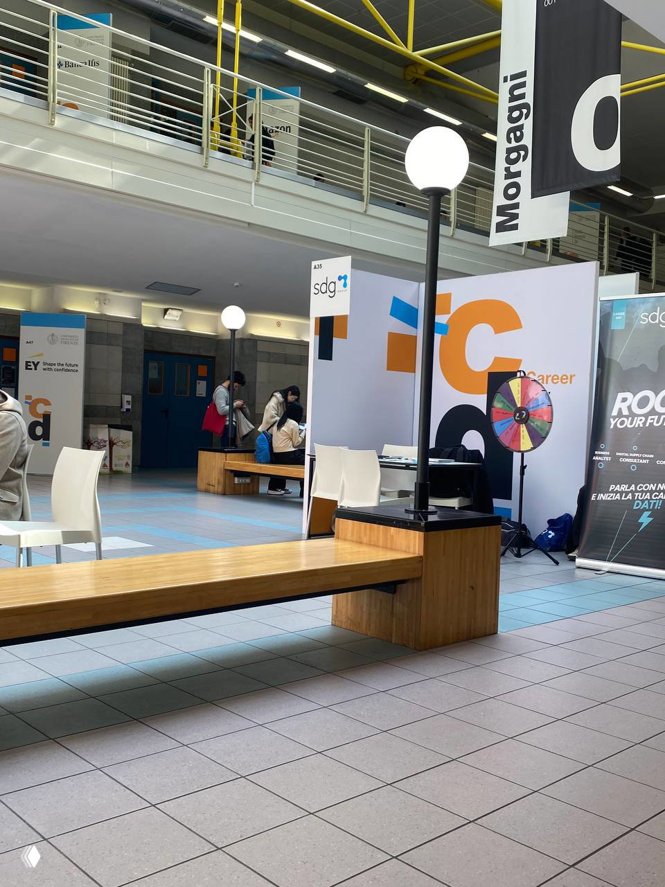 Павильоны Career Day с логотипами компаний, колесо фортуны для посетителей и скамьи в вестибюле — атмосфера рекрутинга и консультаций в университете.