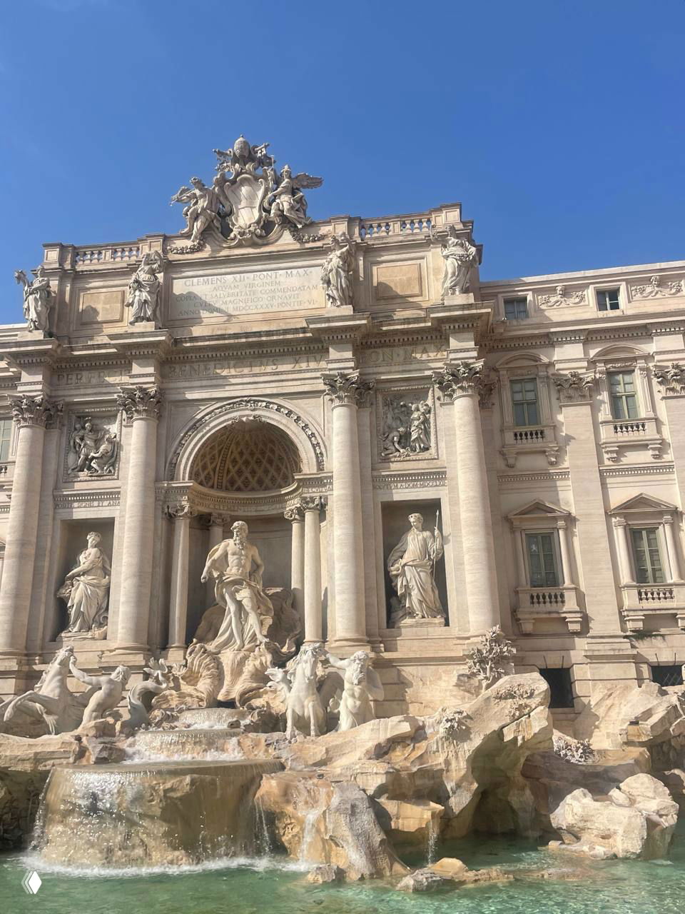 Фонтан Треви крупным планом: монументальный фасад с барельефами и скульптурами, бирюзовая вода в чаше и ясное голубое небо над памятником.