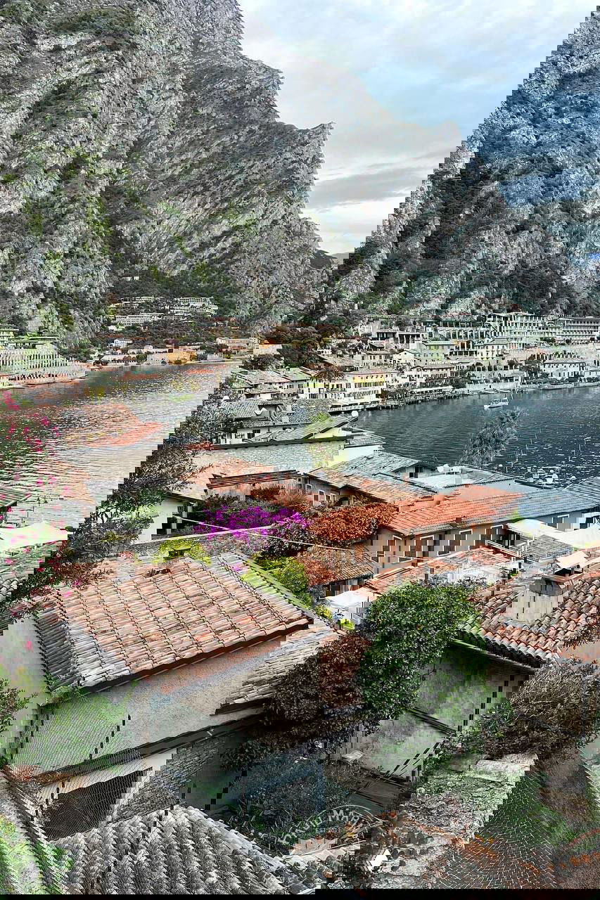 Прибрежная сцена Limone sul Garda на фоне крутого склона: терракотовые крыши, набережная и воды озера Гарда у подножия гор.