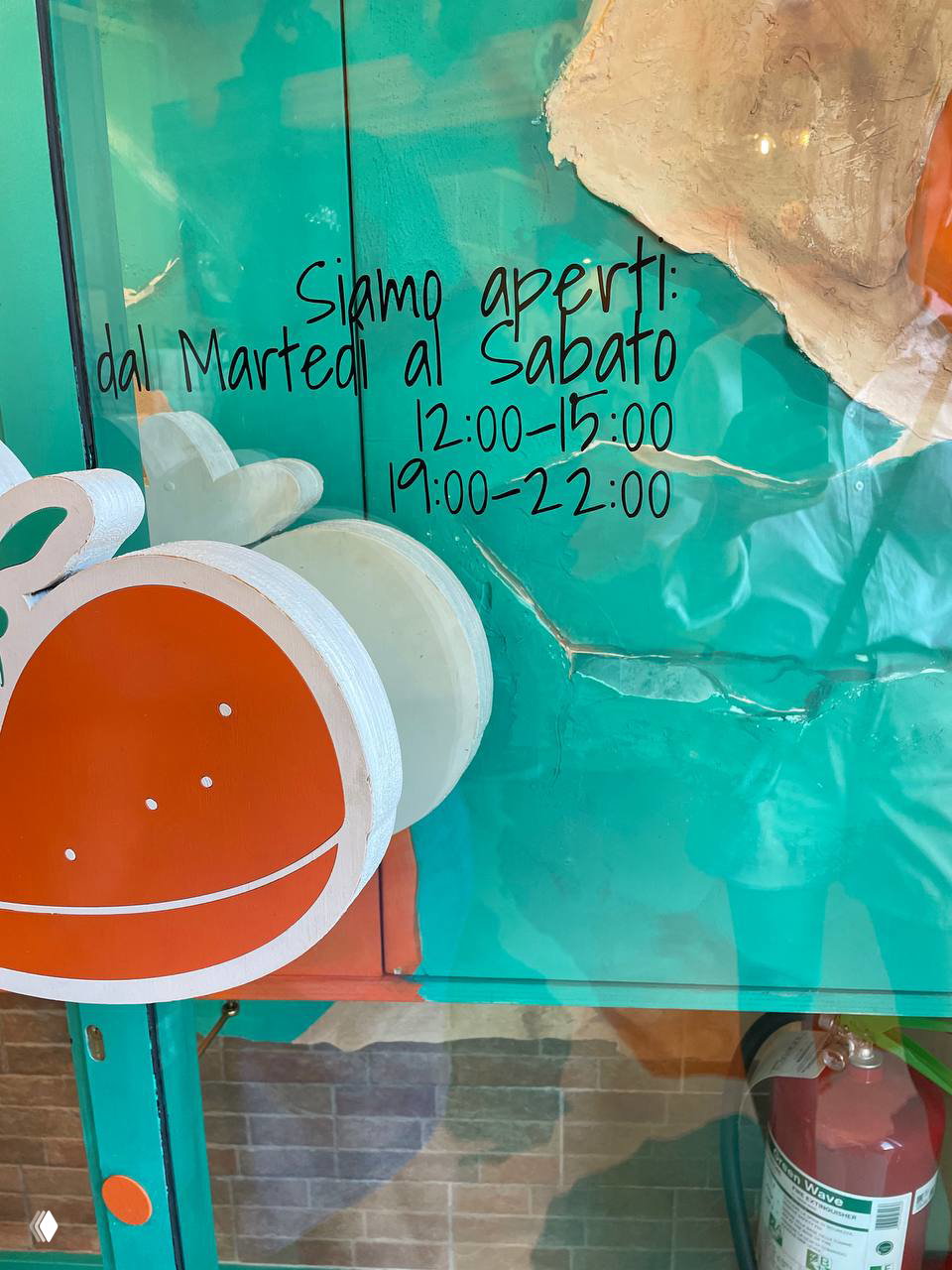 Надпись на стекле с часами работы: «Siamo aperti: dal Martedi al Sabato 12:00-15:00 19:00-22:00» на бирюзовом фоне и декоративный логотип бургера.