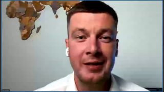 Кадр видеозвонка: мужчина в белой рубашке и наушниках говорит на фоне карты мира; ближний план, студийный фон.