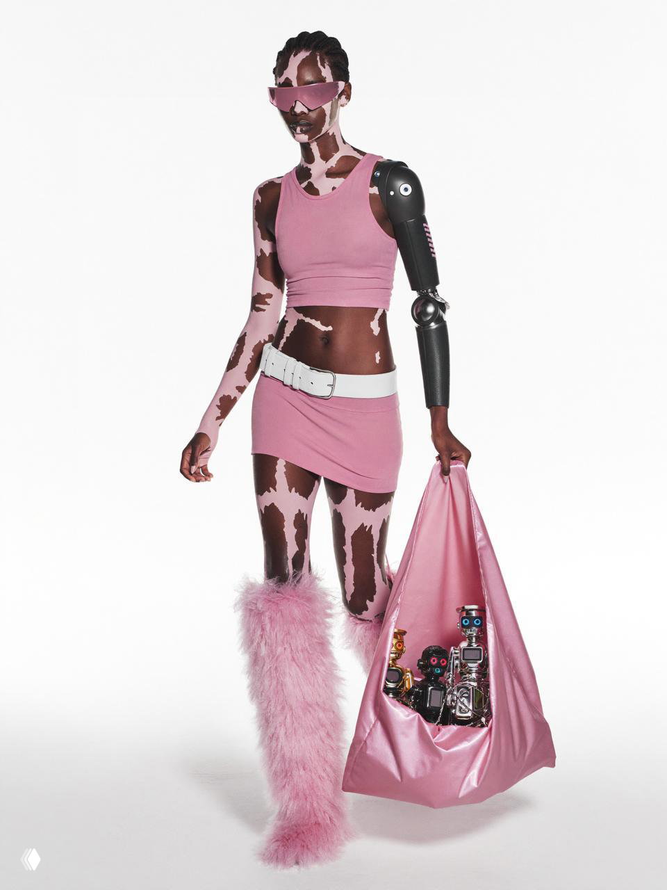 Модель в розовом топе и юбке с протезной рукой и меховыми сапогами идёт с розовым мешком, из которого выглядывают механические игрушки.