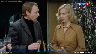 Кадр с мужчиной и женщиной у украшенной ёлки в гостиной; атмосферный кинофрагмент, создающий ощущение вечерней ностальгии и задумчивости.