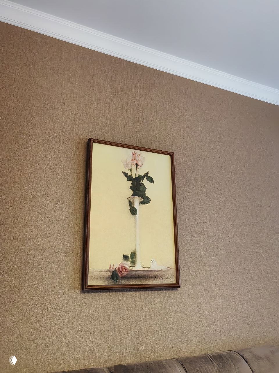 Крупный план картины в раме: бледно-розовые розы в вазе на светлом фоне, висящая на бежевых обоях комнаты.