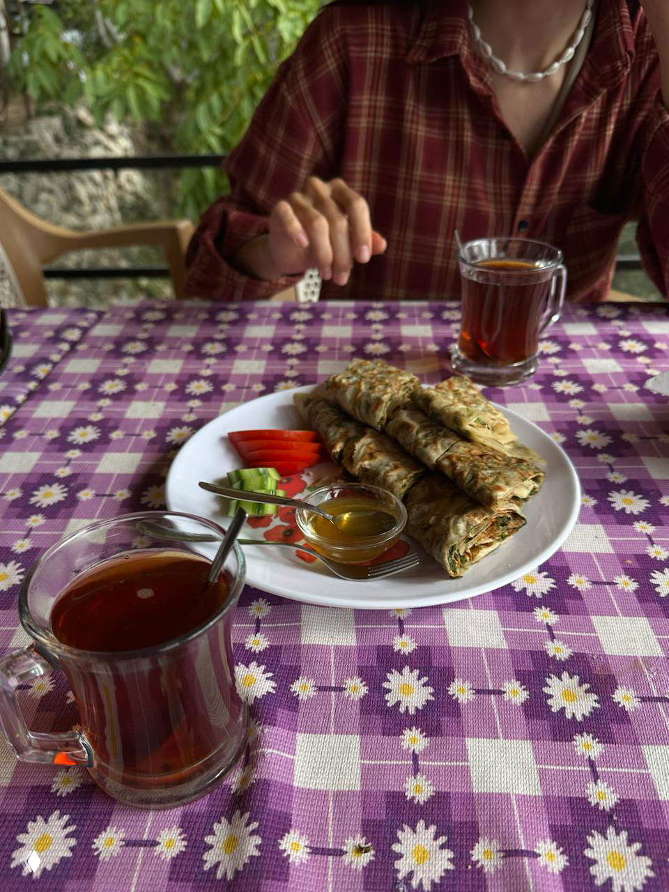 Тарелка со свернутыми свежими лепешками, рядом стаканы с чаем и небольшие добавки — домашняя еда, которую предлагают в деревнях после хайка.
