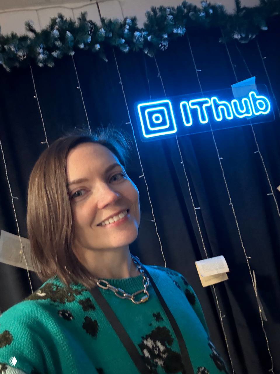 Селфи участницы на фоне неонового логотипа IThub: улыбающаяся женщина и брендовый фон демонстрируют атмосферу пространства.