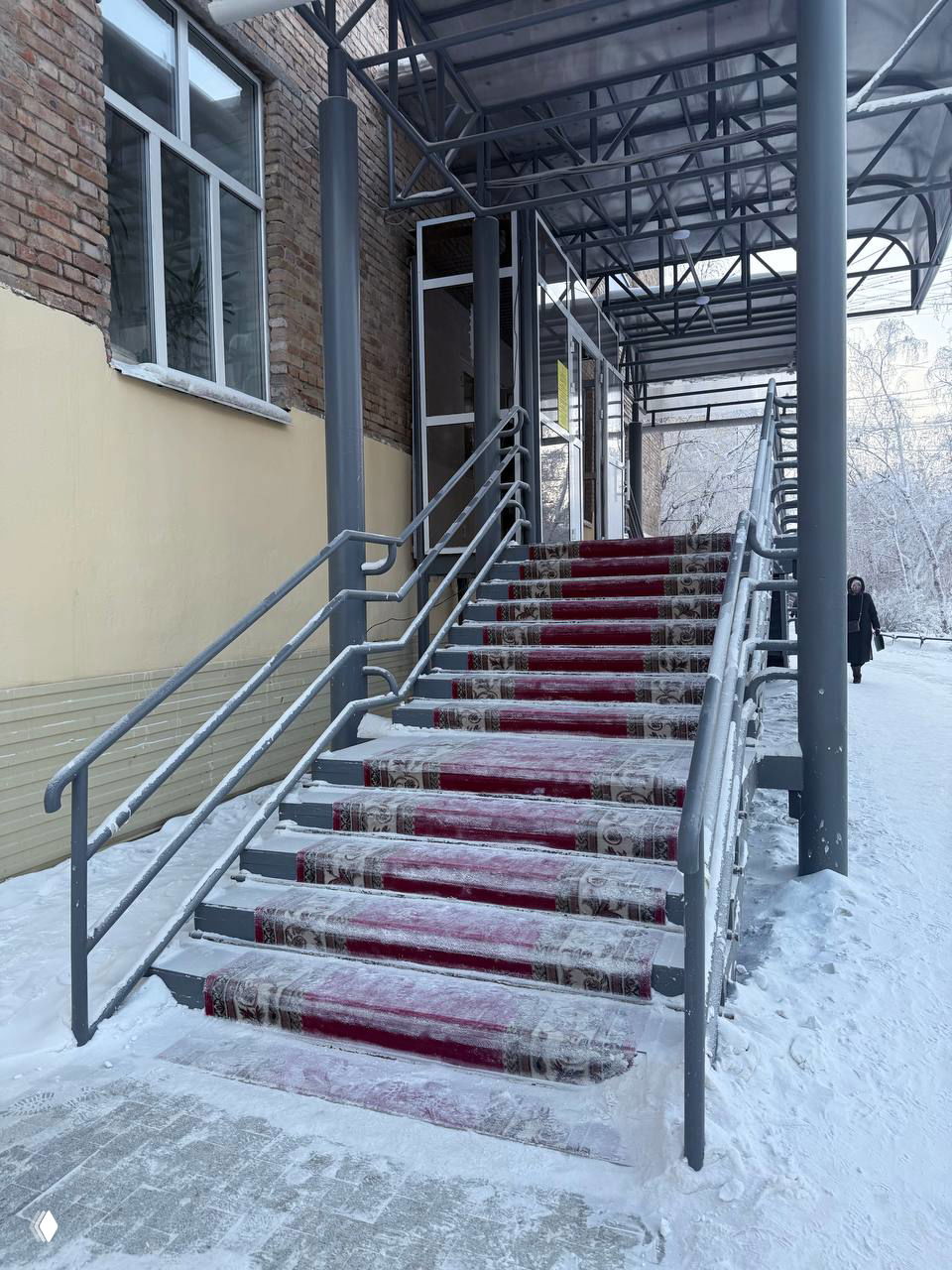Высокая наружная лестница в Якутске с ковровыми дорожками и заметным налётом снега и льда на ступенях — пример архитектурного адаптирования к морозу.