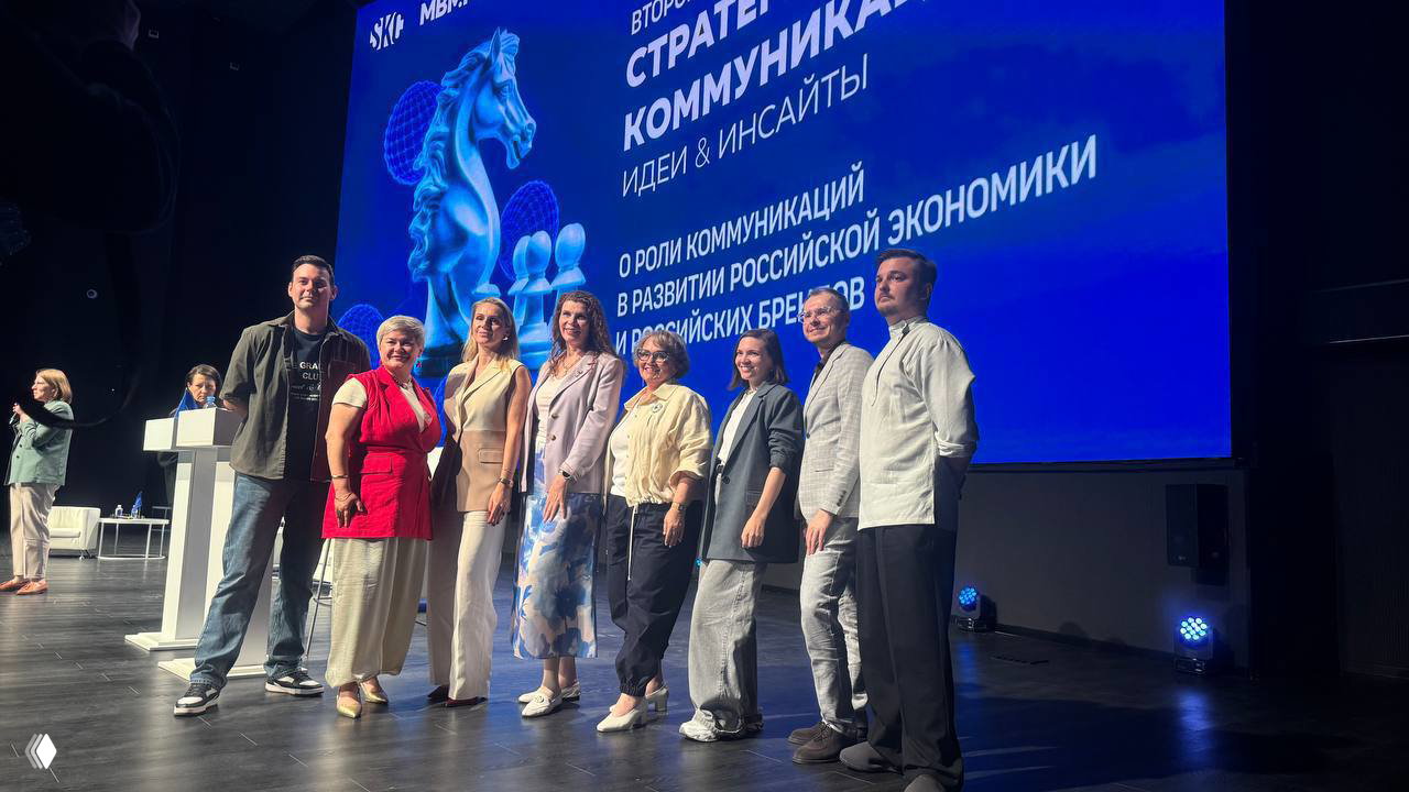 Групповое фото участников сессии на сцене: спикеры и модераторы выстроены в ряд на фоне синего экрана с заголовком форума.