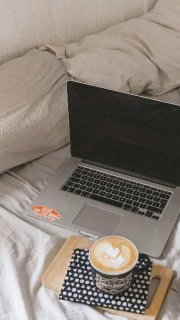 Ноутбук на кровати рядом с чашкой капучино и блокнотом — уютная рабочая обстановка, символ дистанционного обучения и просмотра вебинара.
