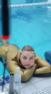 Фридайверша в золотистом гидрокостюме отдыхает у бортика бассейна после статического задержания дыхания; видны очки, снаряжение и вода вокруг.