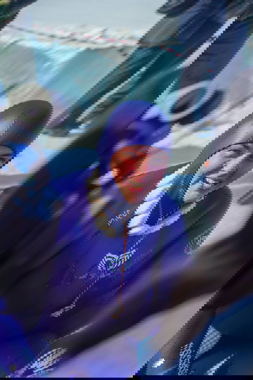 Портрет после погружения: улыбающаяся спортсменка в фиолетовом гидрокостюме с грузом на поясе, рядом камеры и техника, на льду люди.