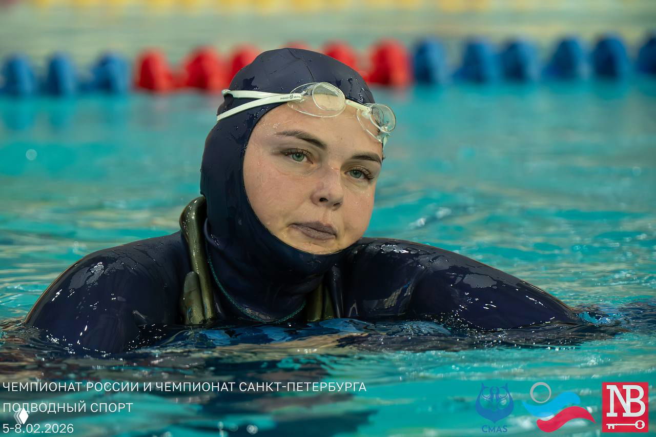 Крупный план спортсменки в гидрокостюме и очках в воде на фоне дорожек бассейна, задумчивое лицо после рабочего нырка на соревнованиях.