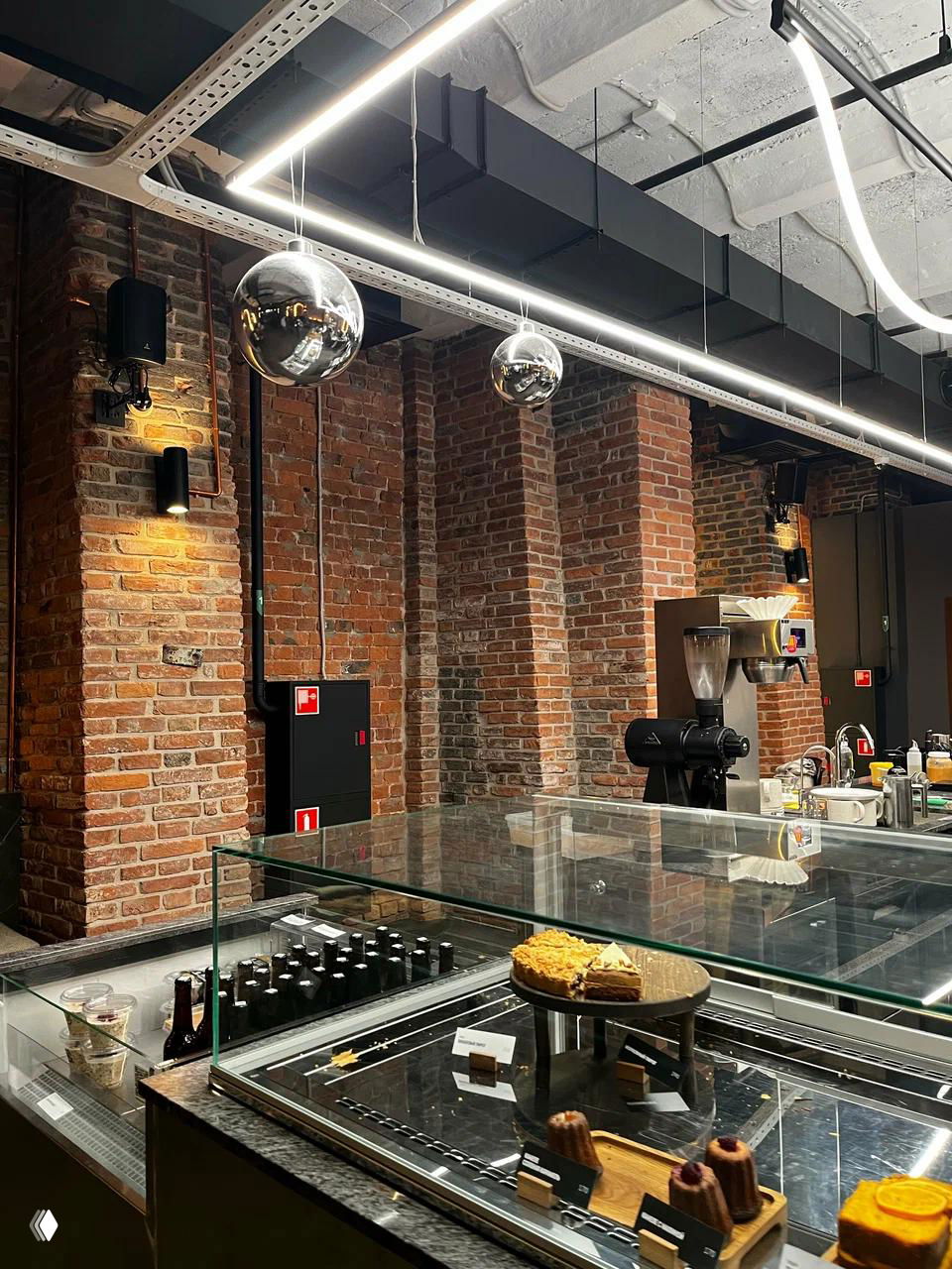 Интерьер в индустриальном стиле: кирпичные стены, витрины с десертами и кофейное оборудование — стильное пространство для работы и перекуса.