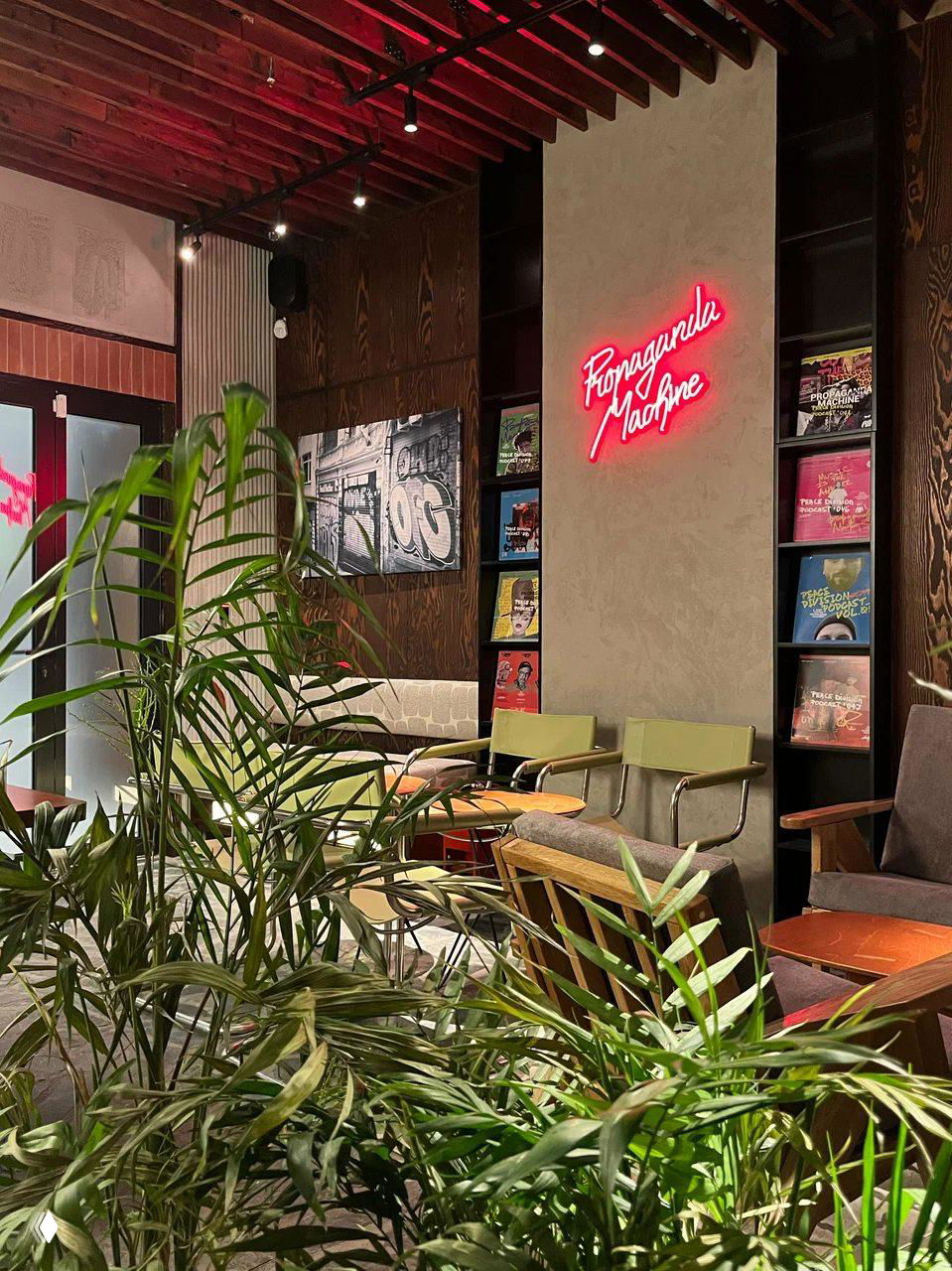 Уютный лаунж-зал с растениями, неоновым логотипом и винтажной мебелью — место с расслабленной атмосферой, подходящее для работы или встреч.