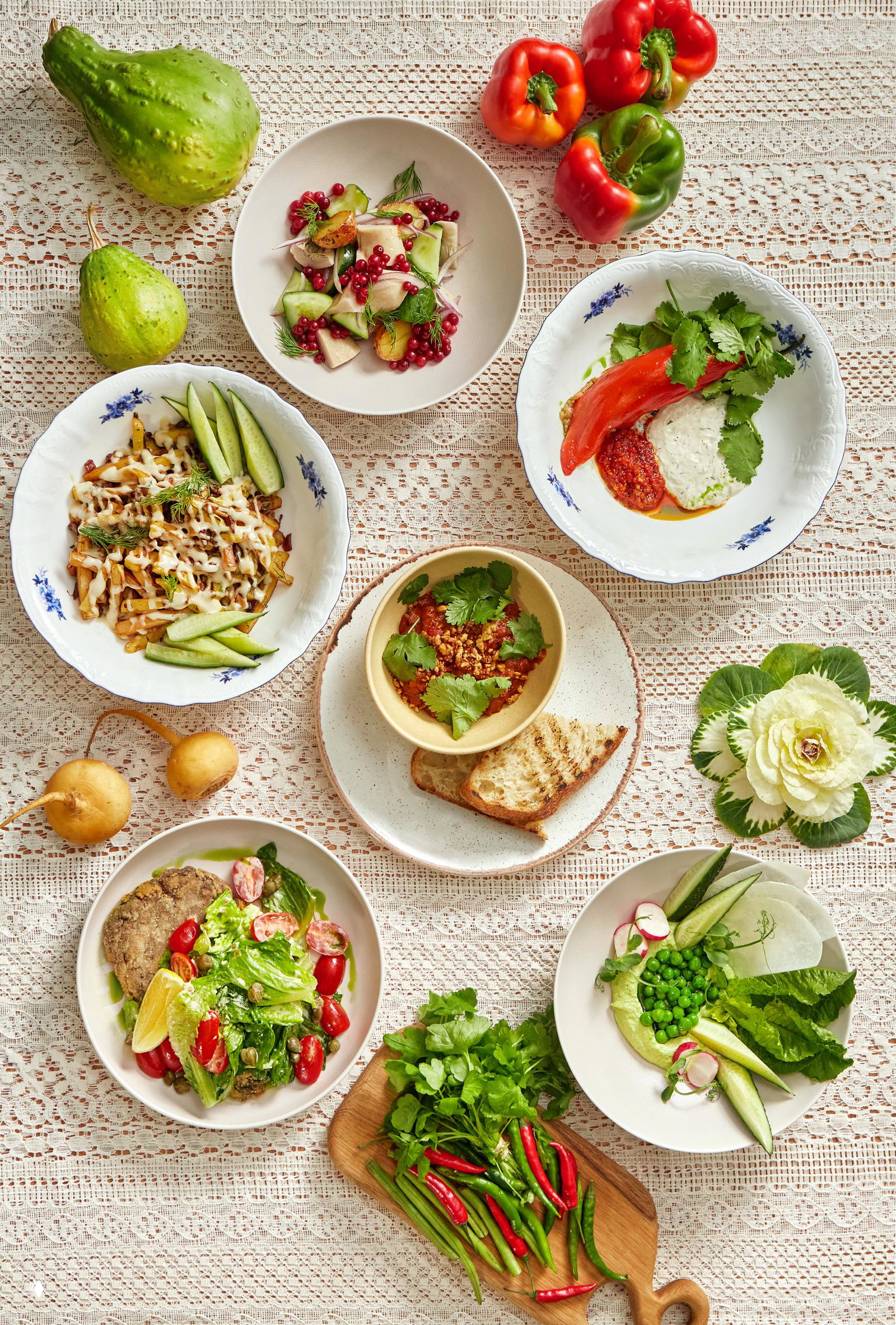 Постные блюда из меню «Банщики»: хумус из зелёного горошка, овощные салаты и закуски с зеленью, подача на кружевной скатерти.