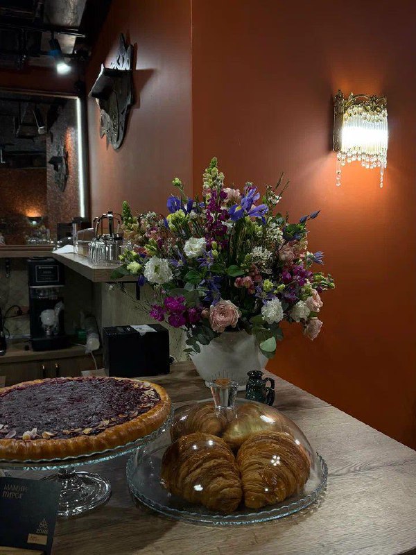 Стол с пирогом и круассанами под стеклянными куполами на фоне большой цветочной композиции и терракотовой стены кафе Empire Zone.