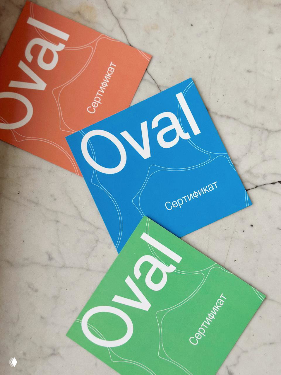 Цветные подарочные сертификаты Oval, разложенные на мраморной поверхности; рекламная полиграфия студии для процедур и уходов.