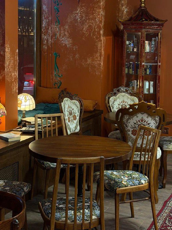 Низкие круглые столы и кресла с узорной обивкой на фоне терракотовых стен; уютный обеденный зал с винтажной мебелью в Empire Zone.