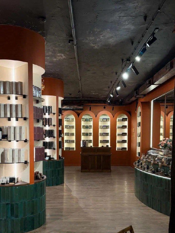 Стеллажи и ниши с флаконами парфюмерии и косметикой на фоне арочных секций и зелёной облицовки стойки в парфюмерной зоне Empire Zone.