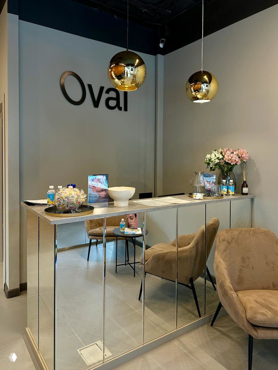Ресепшн студии Oval: зеркальная стойка, мягкие кресла и логотип Oval на стене; зона ожидания и стильный интерьер салона.
