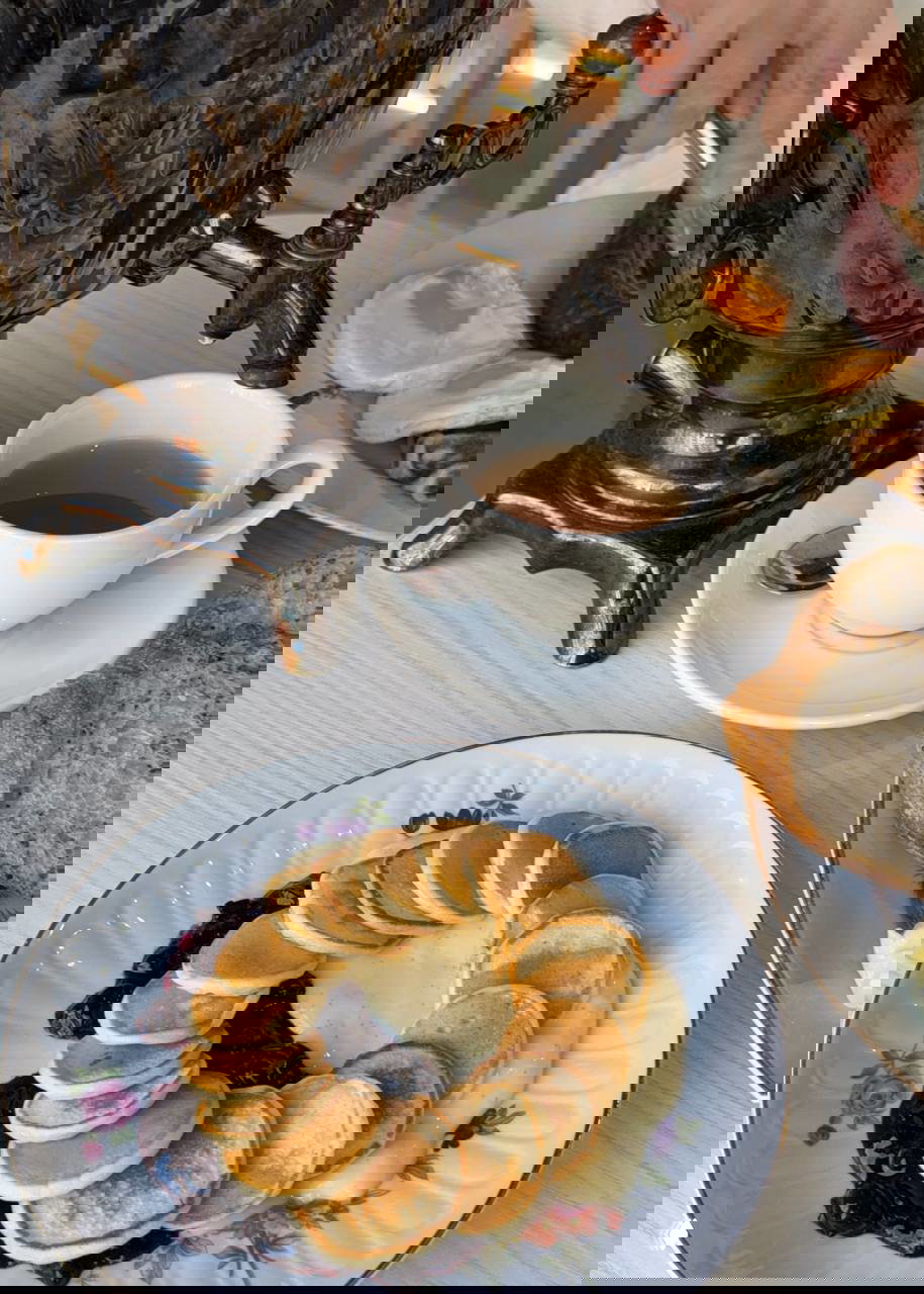 Крупный план самовара, чай в чашке и часть тарелки с яичницей и колбаской — подача традиционного русского завтрака.