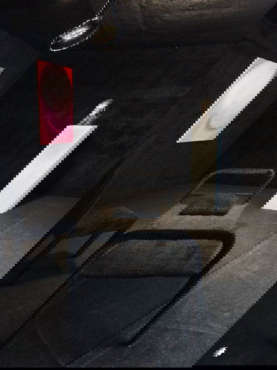 Тёмная инсталляционная комната с обитой чёрной мебелью и пьедесталом со скульптурой — часть сценографии выставки в Anna Nova Gallery.