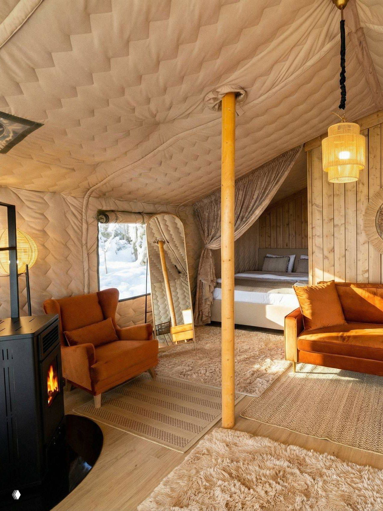 Интерьер палаточного домика Lembo: уютное кресло и диван, работающая печка, кровать и тёплые текстуры в оформлении на фоне окна с видом на снег.