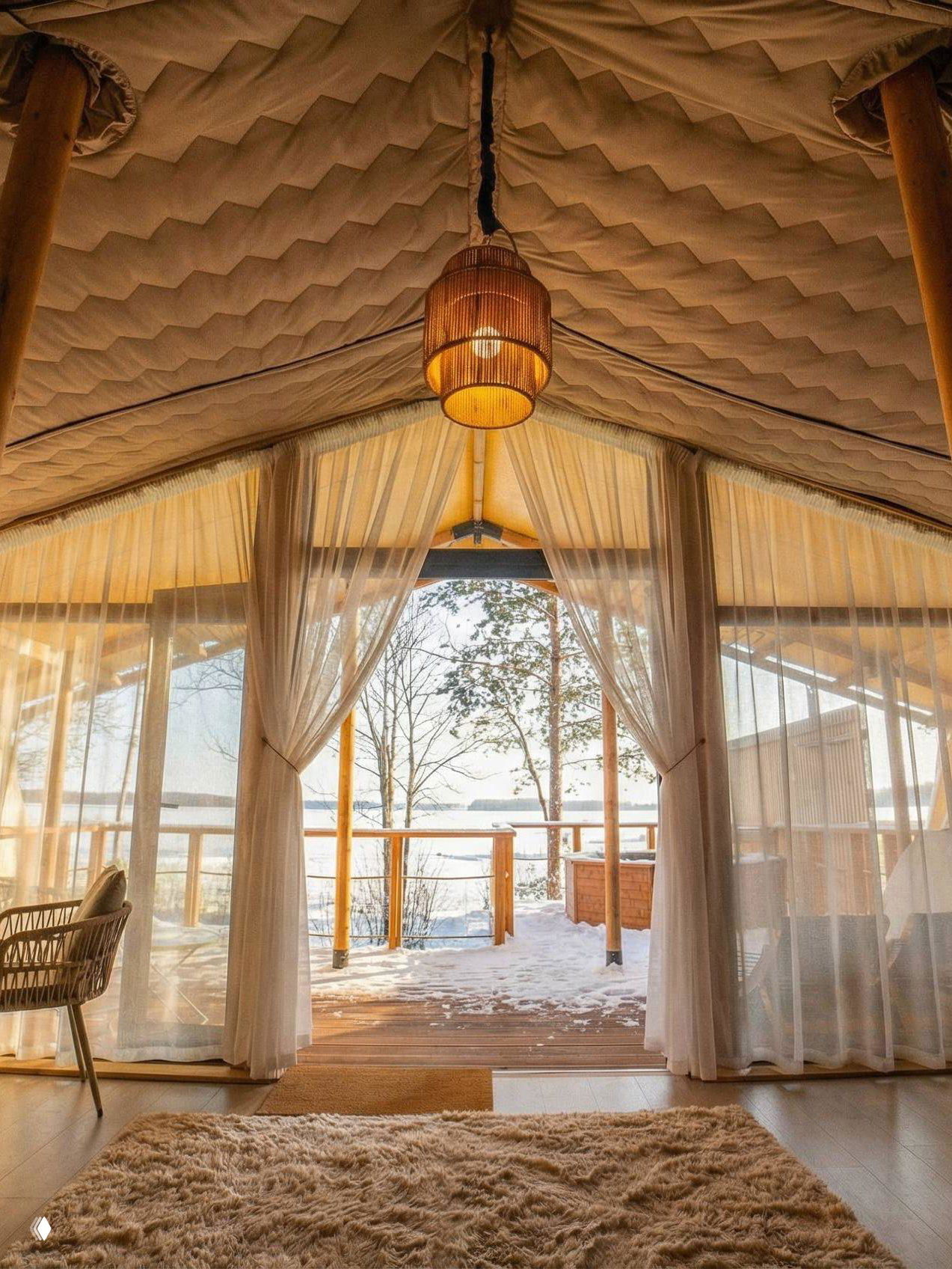 Солнечный вид из палатки Lembo через полупрозрачные шторы: деревянная терраса, снежный берег и спокойное озеро на горизонте в золотом свете.