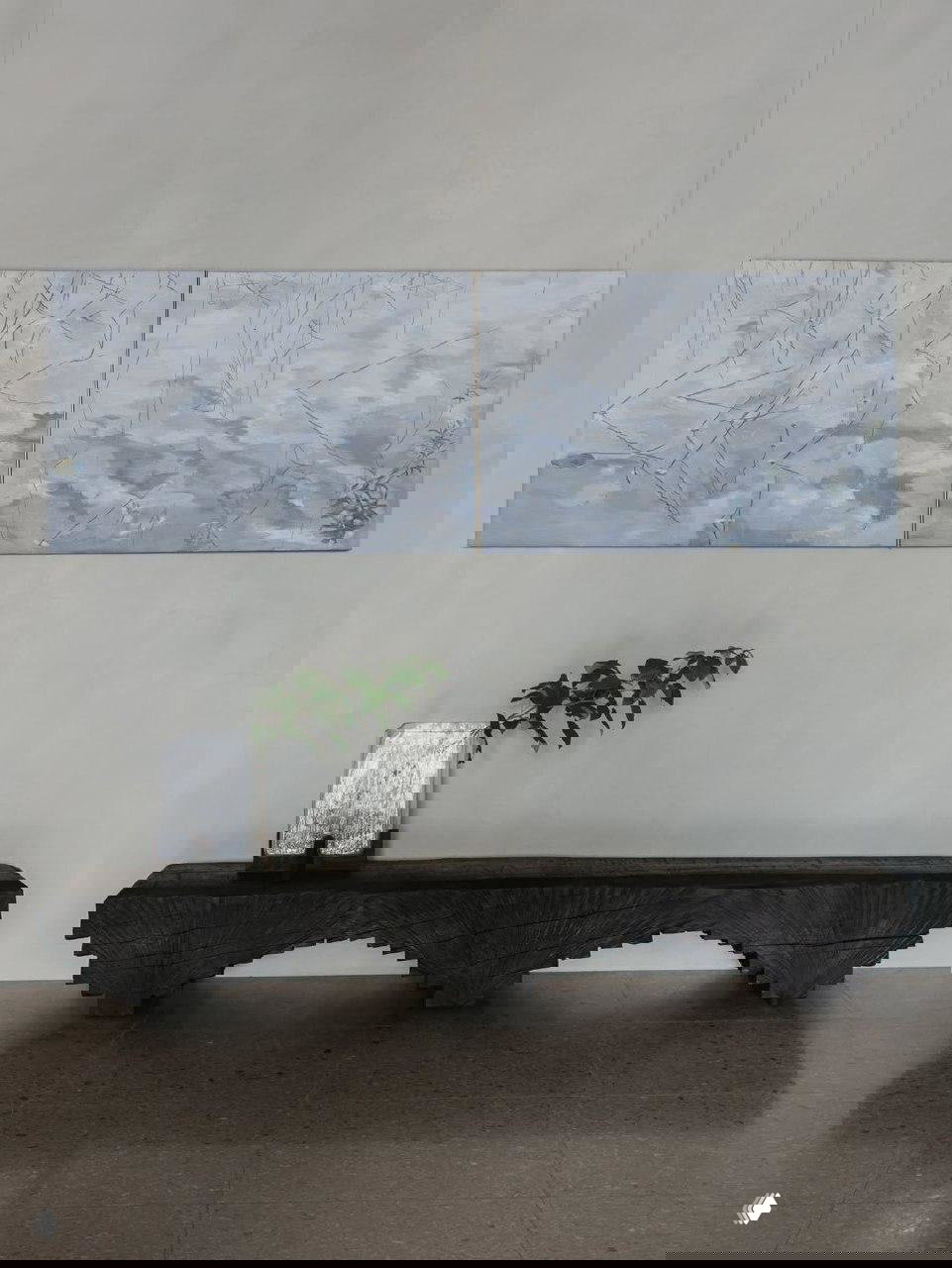 Диптих на светлой стене над низкой тёмной скамьёй; у основания — зеркало и ветка растения, композиция экспозиции выглядит спокойно и созерцательно.