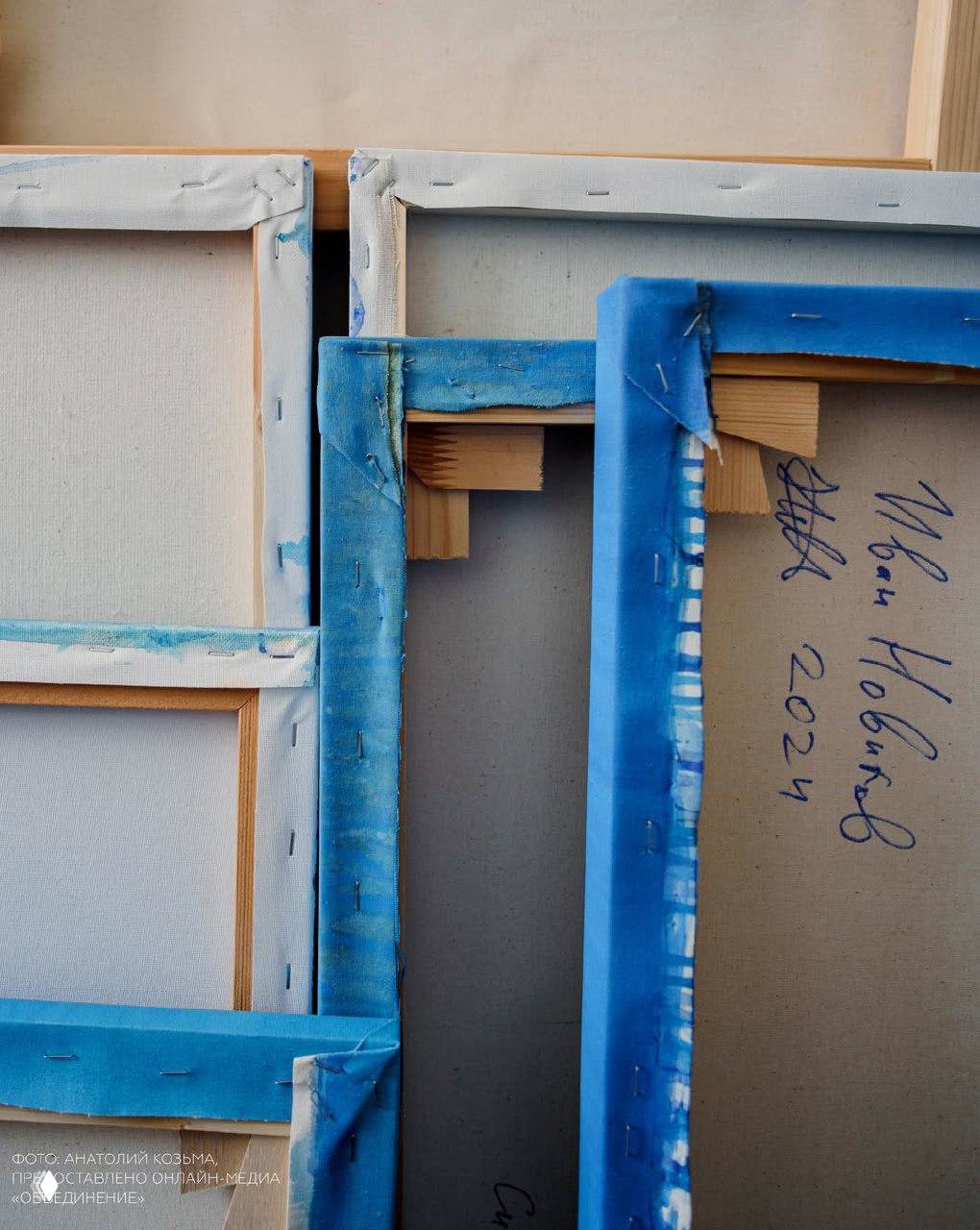 Обратная сторона холстов: вид на натяжку и синие кромки полотна, на картоне различима подпись «Иван Новиков 2024», подготовка экспозиции.