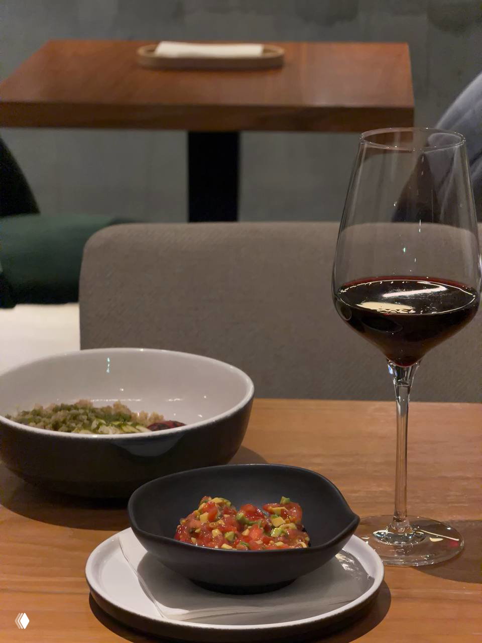 Бокал красного вина и тар-тар из томатов на столе в бистро: крупный план подачи блюда и сервировки в спокойном тёплом освещении.