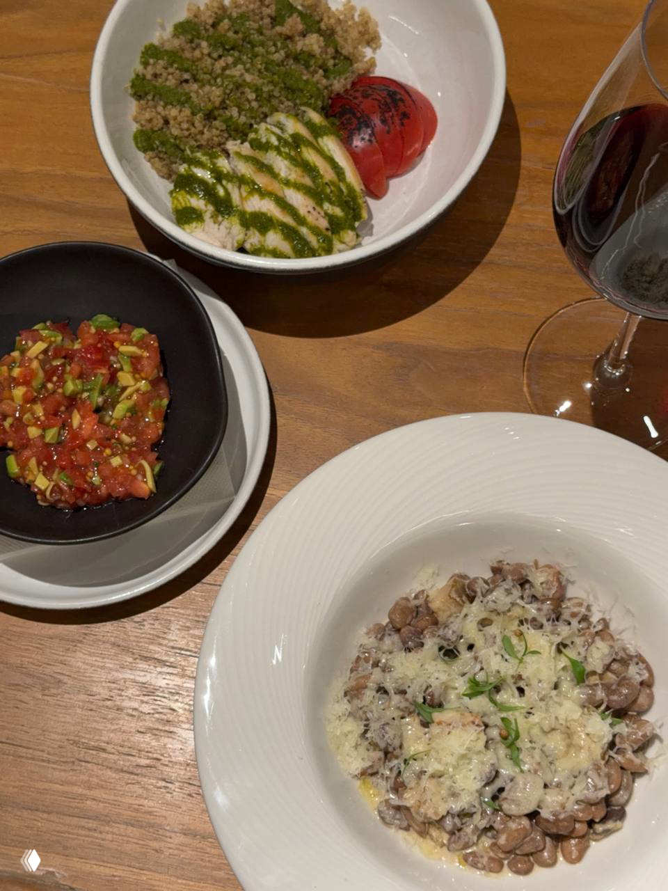 Вид сверху на несколько блюд на деревянном столе: ризотто из белой фасоли, тар-тар и стейк из курицы рядом с бокалом вина.