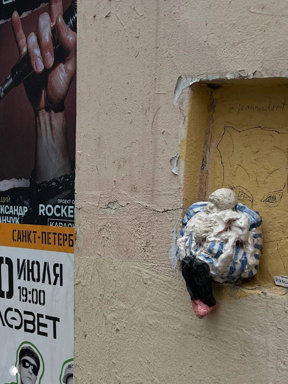 Керамическая фигурка в полосатом кресле или мешке, расслабленная, закреплена в нише рядом с афишей на стене дома; уличные мини-скульптуры Санкт-Петербурга, автор — Екатерина Березина.