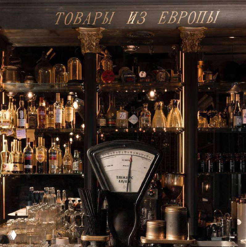 Барная зона Tangiers Lounge с ретро-весами, бутылками и стеклянной посудой на полках, теплое освещение и витрина с напитками и аксессуарами.