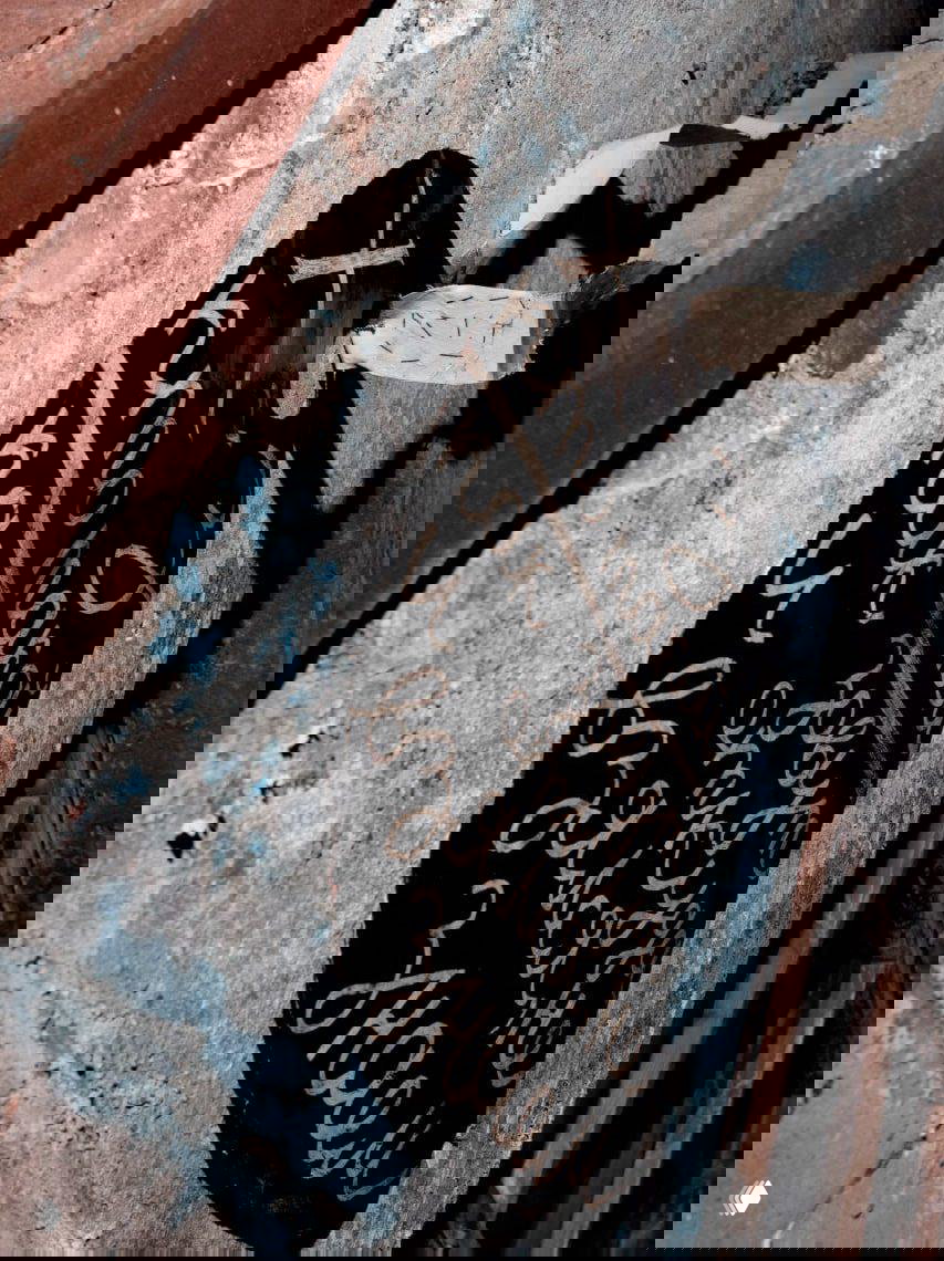 Фрагмент нонконформистской инсталляции: чёрный элемент с белой рукописной надписью на фоне облупленной стены и фактурного пространства.