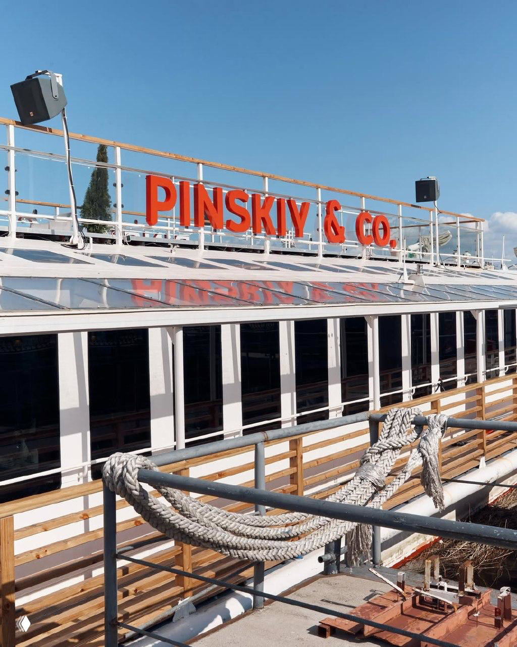 Корпус теплохода с красной надписью PINSKIY & CO, перилами и толстыми швартовыми канатами на причале — место летнего поп‑апа Veter x Tassay.