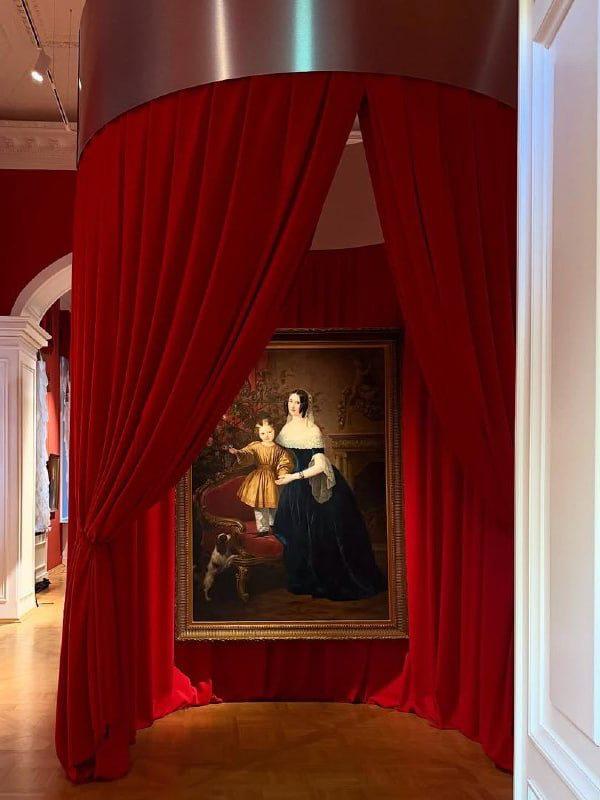 Парадный музейный зал с красными шторами и раритетным портретом в рамке — торжественная музейная инсталляция в классическом интерьере.