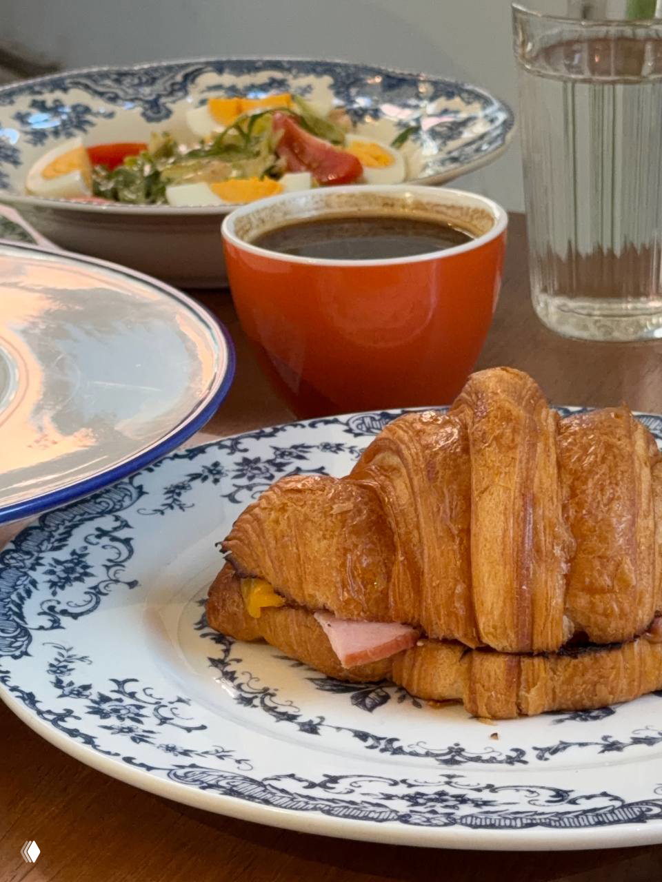 Круассан с окороком на узорчатой тарелке, рядом чашка кофе и салат — фото блюда из основного меню 8:am.