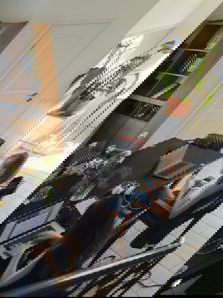 Общий вид рабочего пространства: большой стол, несколько ноутбуков, люди за работой, растения и светлый интерьер, ощущение совместной работы.