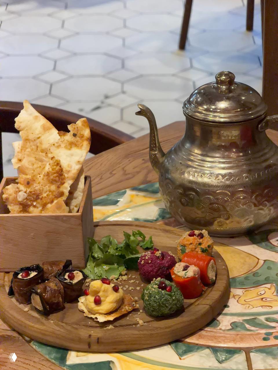 Деревянная доска с грузинскими закусками: рулеты из баклажанов, шарики из сыра с гранатом, овощные роллы и хрустящий лаваш рядом с металлическим чайником.