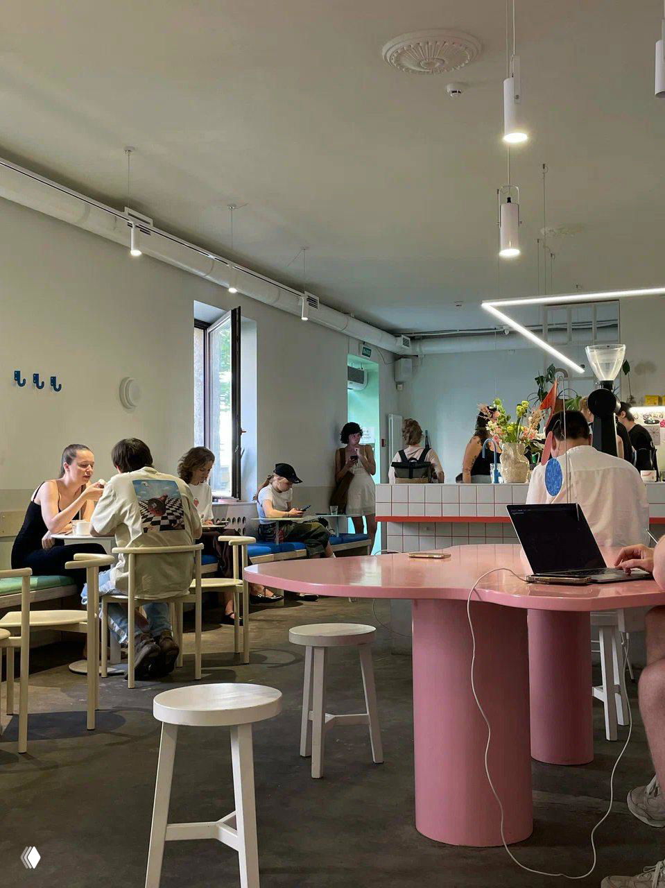 Современное светлое кафе: посетители, барная стойка, молодая публика и столы с розетками — место с оживленной атмосферой и возможностью подключить ноутбук.