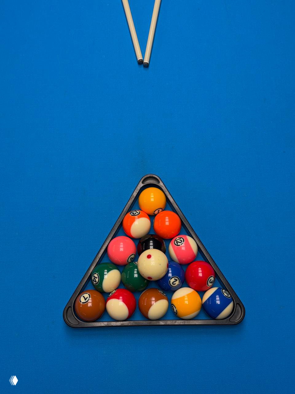 Треугольник с аккуратно расставленными разноцветными шарами пула на ярко‑синем сукне стола, вид сверху перед началом партии.