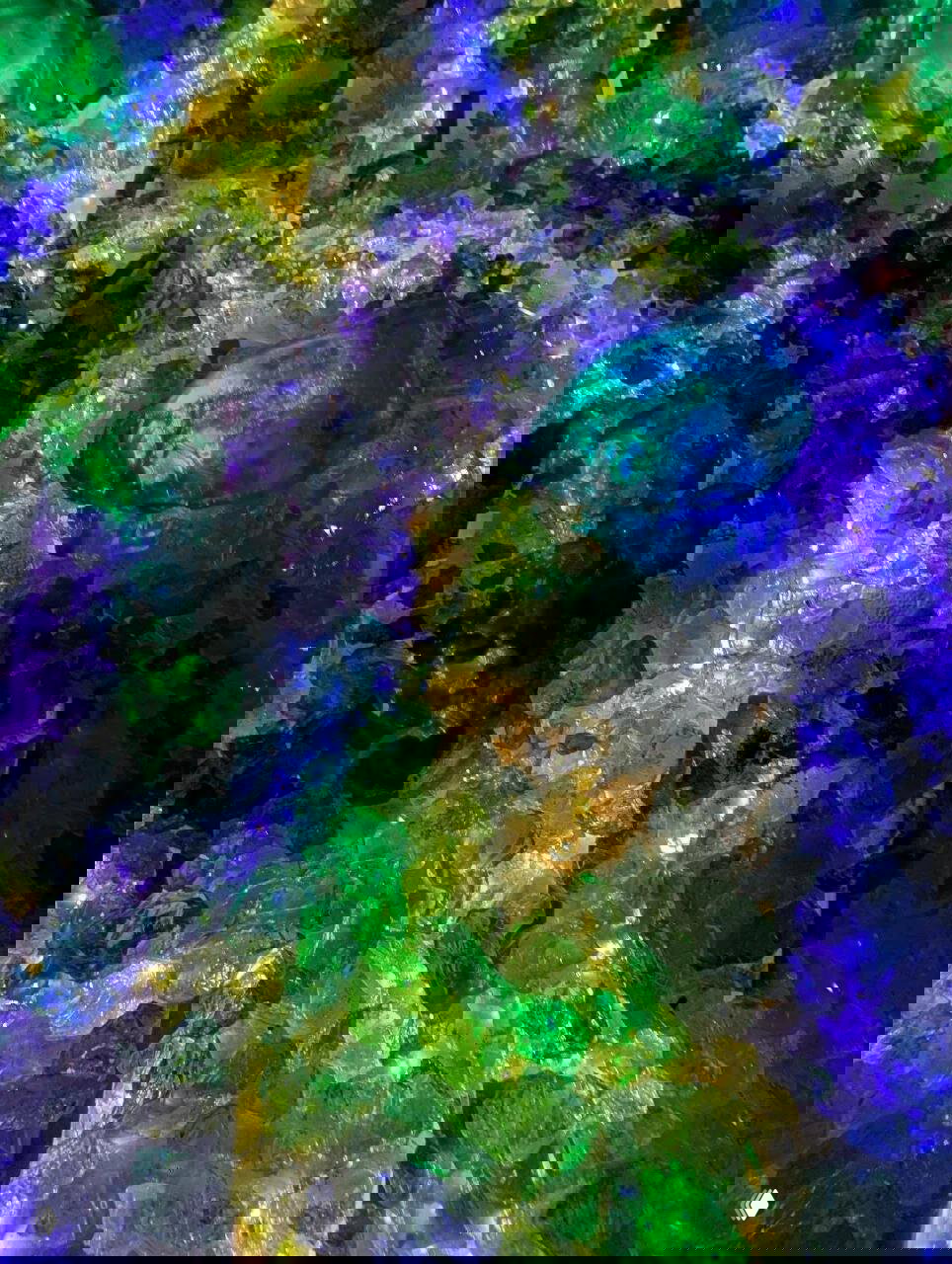 Крупный план подсвеченных кусочков стекла и имитации кристаллов с зелёными и фиолетовыми акцентами в напольной инсталляции.