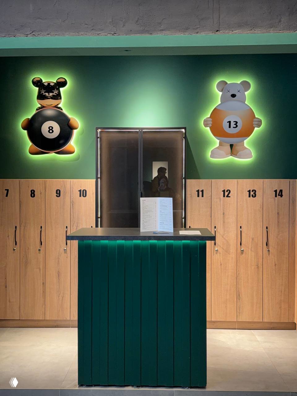 Ресепшн с зелёной стойкой и пронумерованными шкафчиками за ней, над стойкой светящиеся декоративные фигурки с шарами «8» и «13».