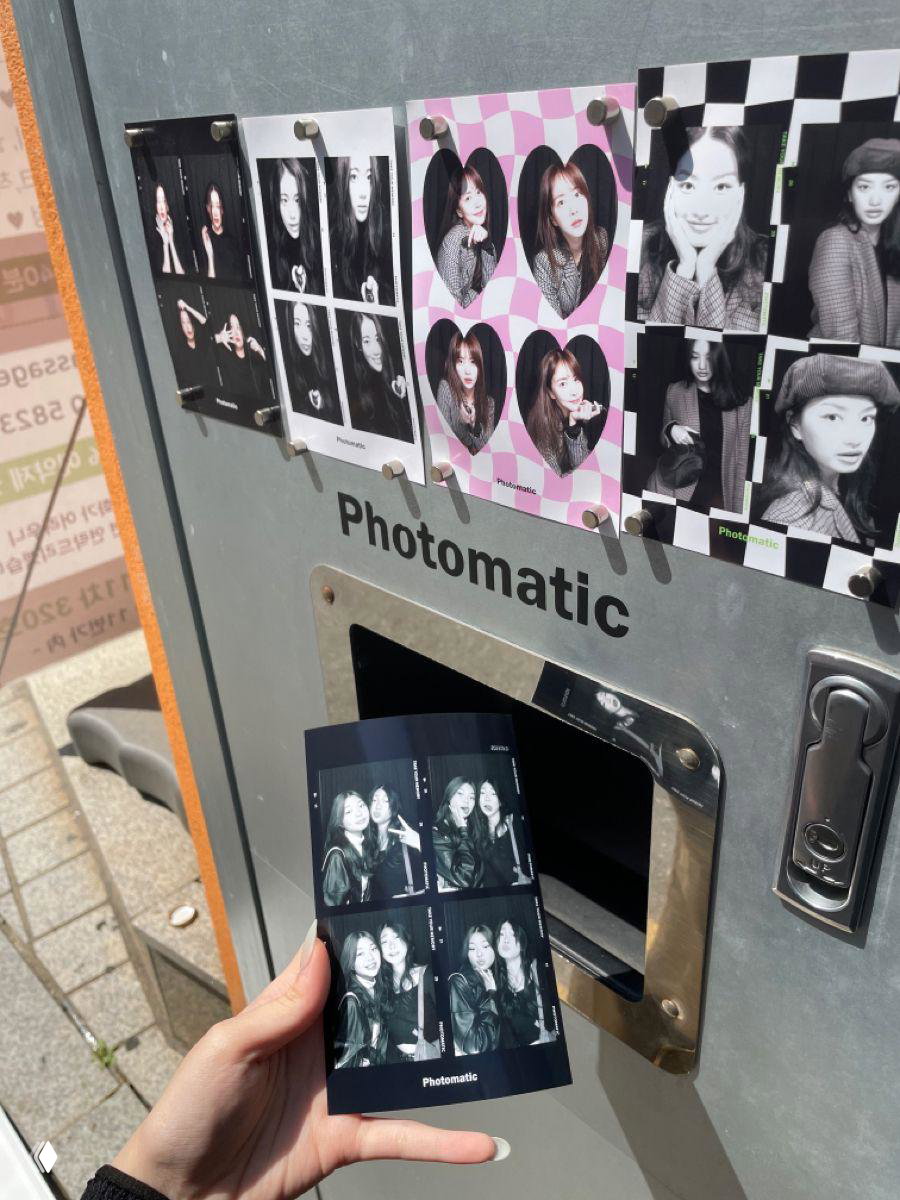 Лист фотополосок из фотобудки (Photomatic), рука держит черно‑белые снимки на фоне автомата — элемент уличной культуры и развлечений.