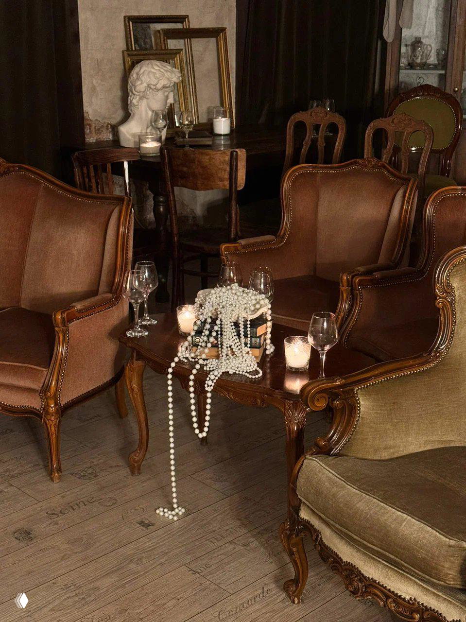 Гостиная с кожаными креслами, бокалами, свечами и нитями жемчуга на столике — сцена перед кинопоказом или встречей.