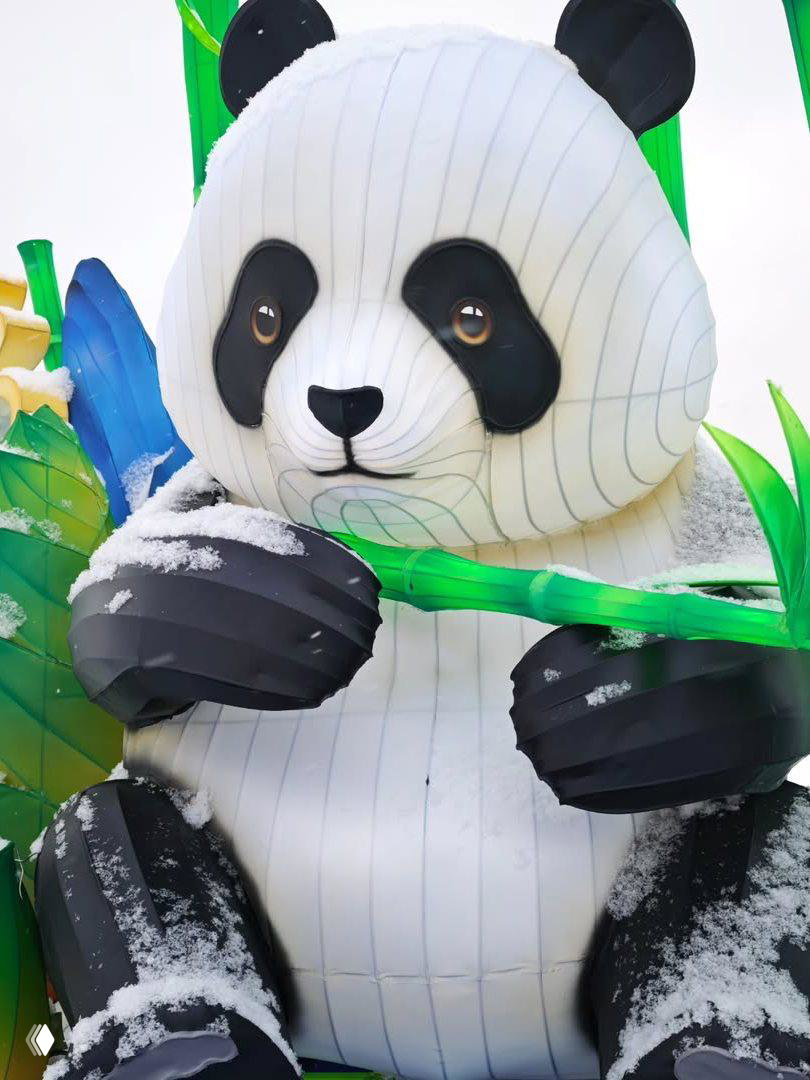 Большая светящаяся фигура панды из тканевых фонарей с ветками бамбука, на которой видны снежные хлопья в оформлении фестиваля.