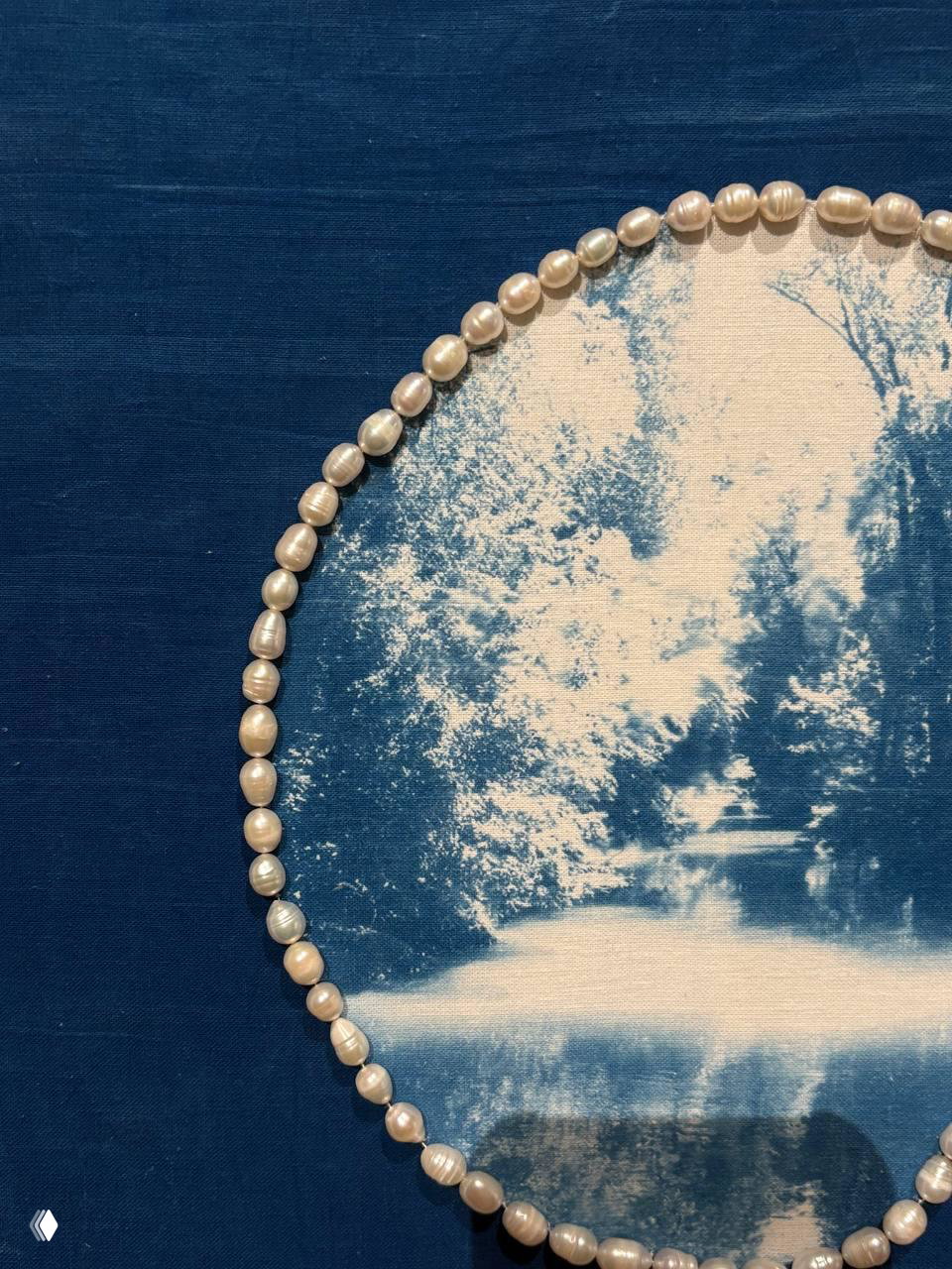 Крупный план: голубой отпечаток на ткани, по краю вручную пришиты речные жемчужины, видны текстура ткани и бусины.