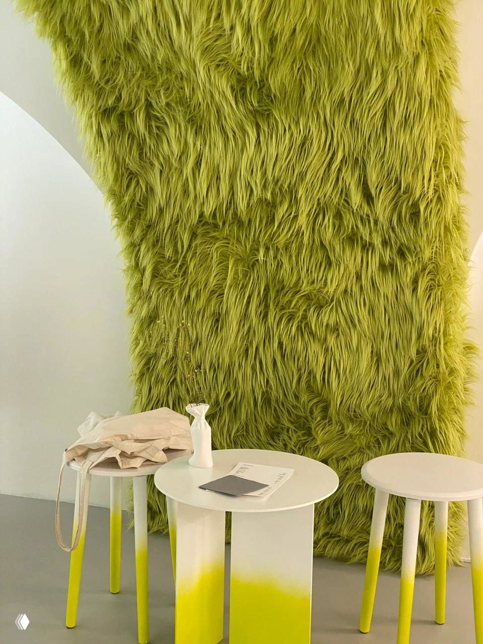 Крупный ракурс зелёной пушистой стены в магазине Fjord рядом с белым круглым столиком, вазой и табуретом — ощущение текстуры и цвета.